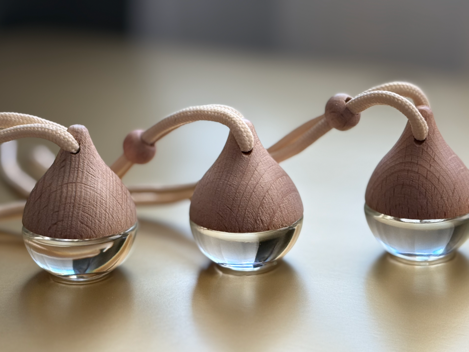 Three car diffusers with wooden top and glass base standing on a reflective surface with a blurred background