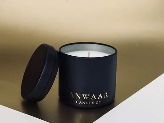 Black candle jar with a white candle inside, featuring 'ANWAAR CANDLE CO' branding, on a beige background.