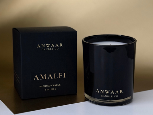 Black candle with 'Anwaar Candle Co' branding next to its packaging on a beige background