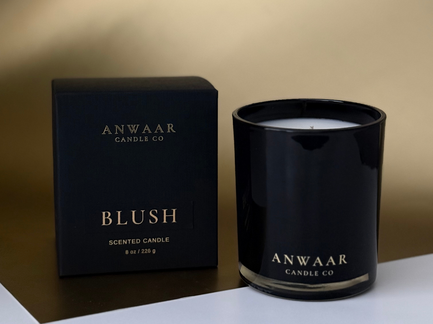 Black candle and packaging with 'Anwaar Candles Co' branding on a gold background