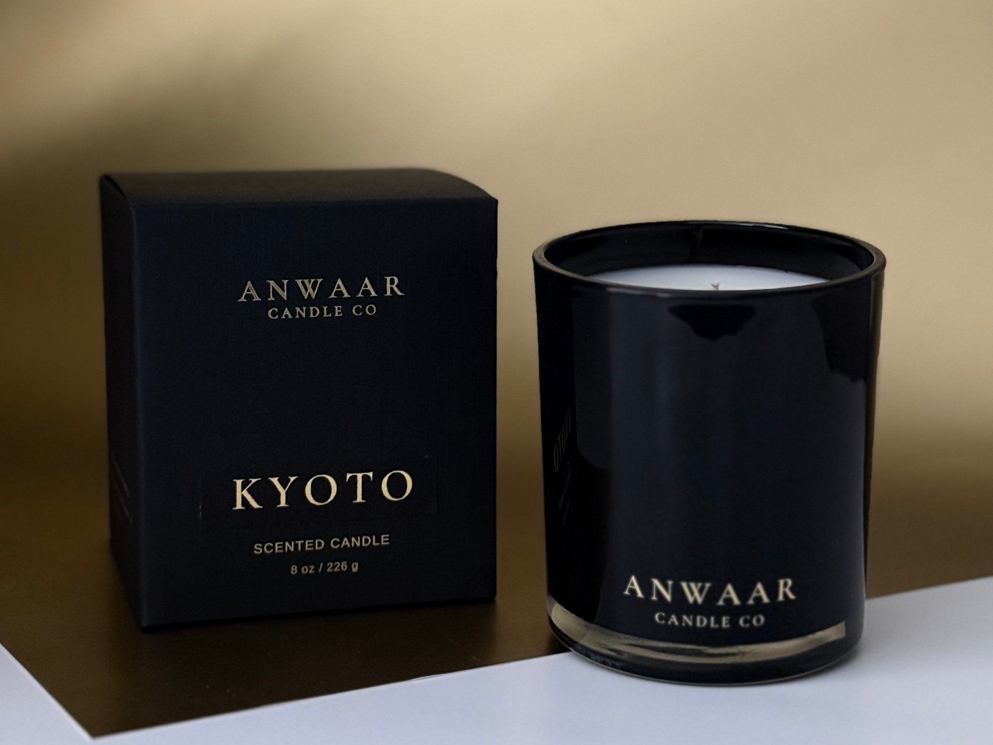 Black candle with 'Anwaar Candle Co' branding next to its packaging on a white surface.