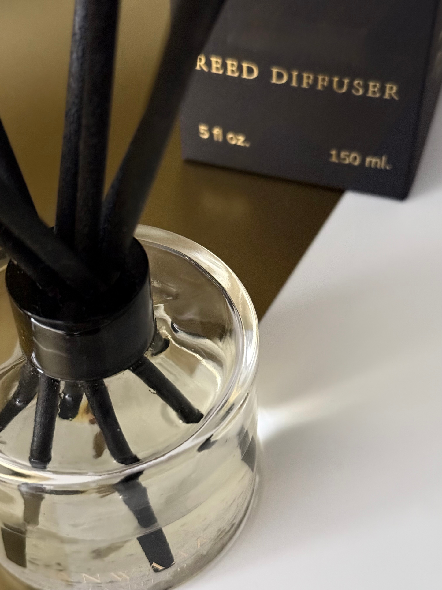 Reed diffuser with black reeds and clear base on a white surface.